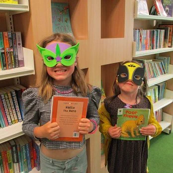 two girls wearing superhero masks holding books