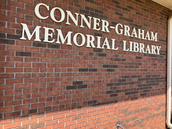 The sign for the Conner-Graham Memorial Library, hanging on a brick wall.