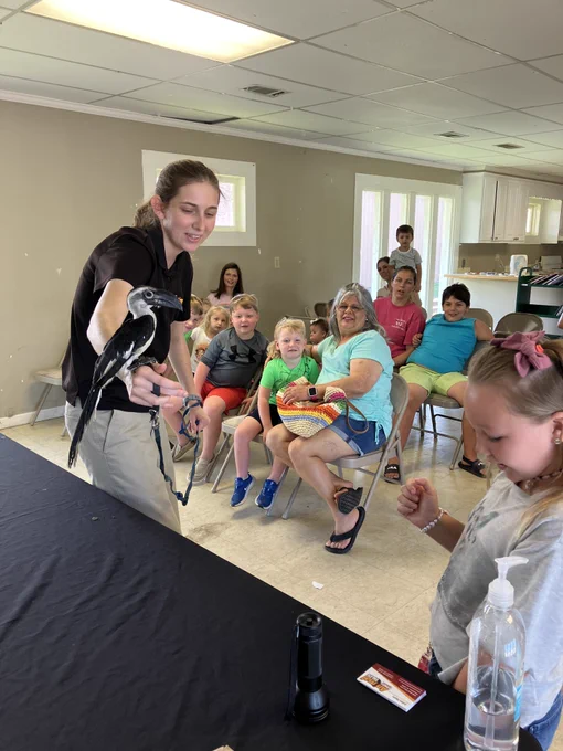 A white woman holds some sort of small exotic bird. Parents and children look on, watching her and the bird.