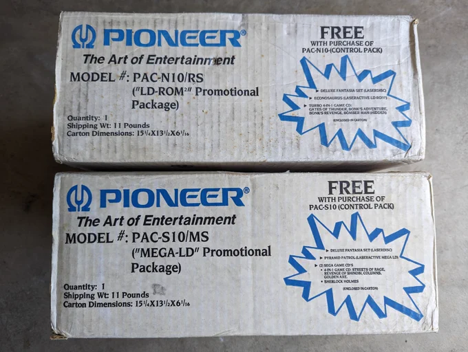 Two white Pioneer labeled boxes on the floor. The top box is a model PAC-N10/RS ("LD-ROM" Promotional Package and FREE with purchase are a Deluxe Fantasia LaserDisc, Econosaurus LD, and Turbo 4-in-1 CD with Gates of Thunder, Bonk's Adventure, Bonk's Revenge, Bombmer Man (Hidden). The second box is a model PAC-S10/MS ("Mega-LD" Promotional Package) and FREE with purchase is the Deluxe Fantasia Laserdisc, Pyramid Patrol, and 2 Sega Game CDs, a 4-in-1 with Streets of Rage, Revenge of Shinobi, Columns, and Golden Axe and a Sherlock Holmes CD.