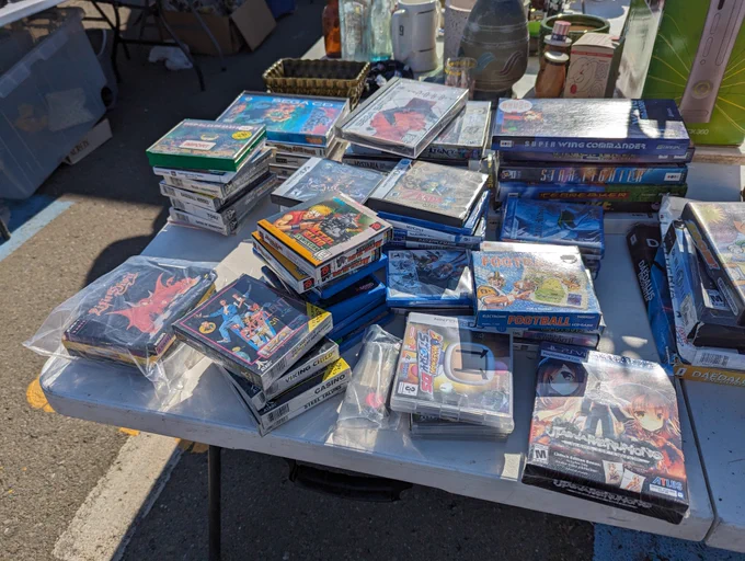 A table with stacks of video games including sealed Atari Lynx games, CD-i discs, Metal Slug First Mission for Neo Geo Pocket, some 3DO titles, and scattered DS, PS Vita, and Saturn games.