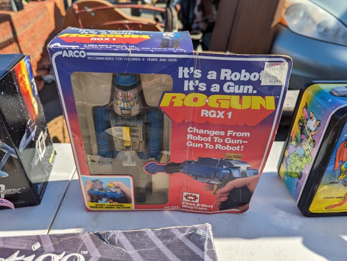 A boxed Arco Ro-Gun RGX 1 toy. It's a robot that turns into a gun that fires the old ring caps. The box reads: It's a Robot. It's a Gun. Changes from Robot To Gun - Gun To Robot. It also has the Kay-Bee price sticker $6.99