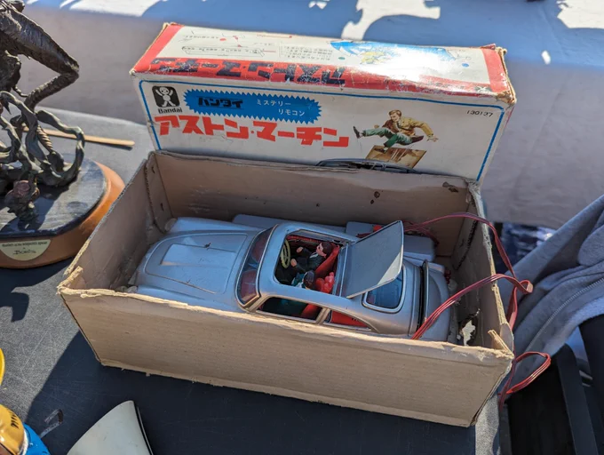 A boxed Japanese Bandai Aston Martin toy. It has a roof on a hinge and an attached remote allows you to deploy forward-facing guns and eject one of the seated figures. A James Bond toy in everything but name.