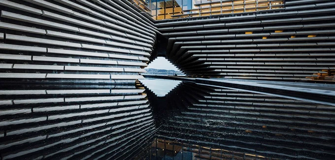 A photo of V&A Dundee, the building is reflected in the pool of water.