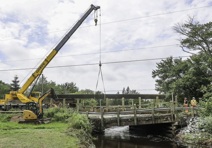 A crane operator moves lumber to repair a bridge