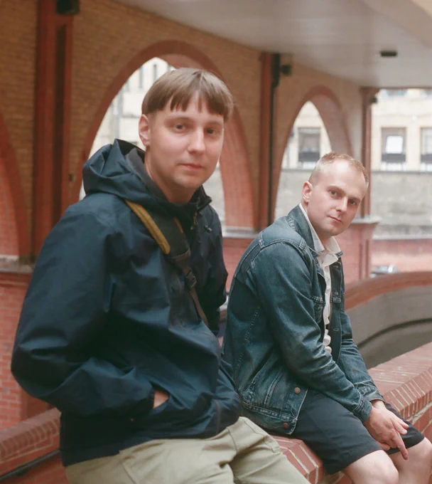 Photo of Simkin and DJ Pitch sitting on a red brick wall