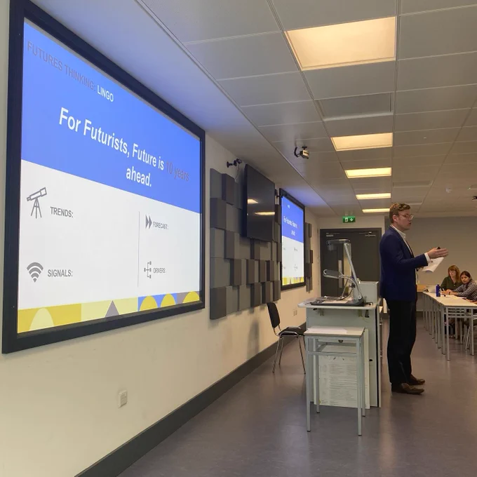 L&D Specialist giving classroom session on Futures Thinking with presentation projected onto screen. 