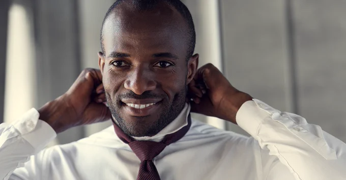 A person in a white collared shirt puts on a dark red neck tie.
