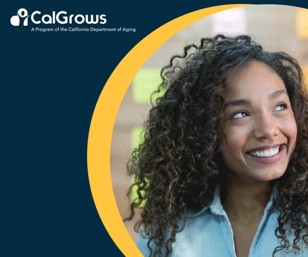 A young Black woman smiling in front of a board of Post-It notes. 