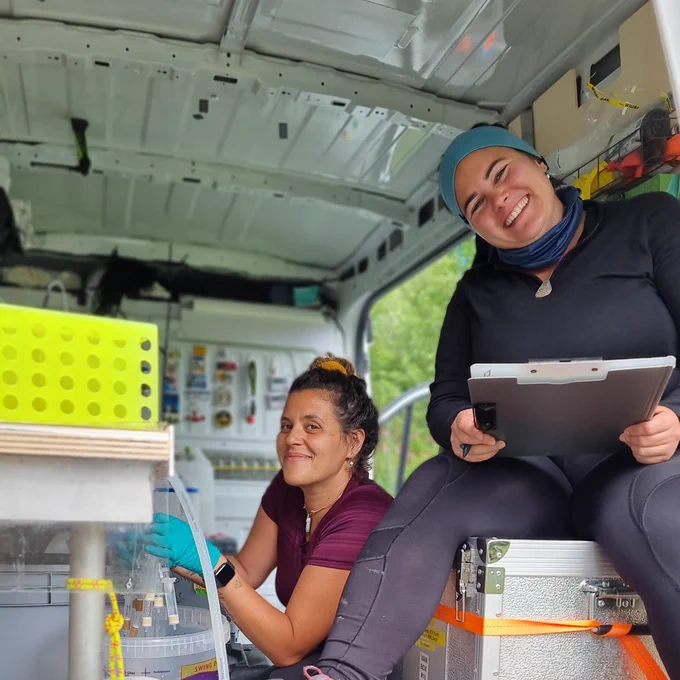 Two participants of the EMBL TREC expedition smile to the camera while working in the EMBL mobile laboratory.