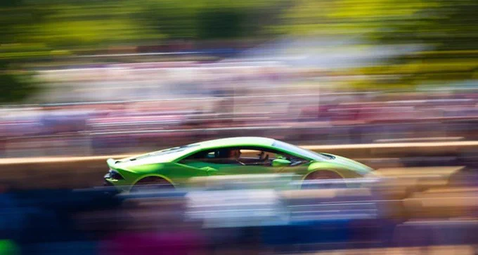 Photograph of a green coloured supercar racing on a track.
