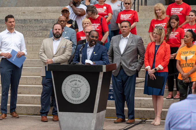 Senator Craig standing at a podium delivering remarks in front of the Statehouse with other leaders.