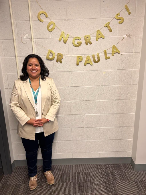 Paula standing beside a congratulations banner after a successful PhD final exam / thesis defence.