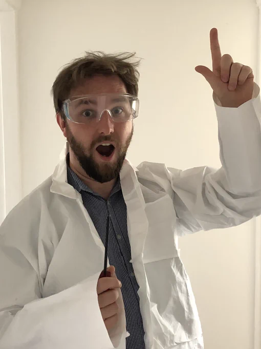 A photograph of Alastair wearing a lab coat and safety goggles, and holding a screwdriver. He’s stood in a eureka pose, with a shocked expression on his face