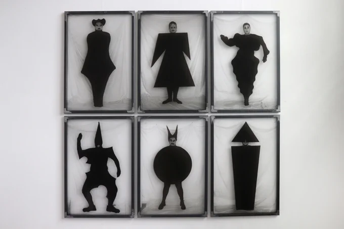 A series of 6 screen print frames on a wall containing figures dressed in bold black shapes. 