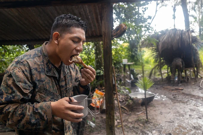 U.S. Marine Corps Lance Cpl. Jonathan Lojacalle, a rifleman with Fox Company, 2nd Battalion, 25th Marine Regiment, 4th Marine Division, Marine Forces Reserve, takes a bite of chicken during the Jungle Amphibious Training School as part of Tradewinds 2023 at the Jungle Area Training Site in Guyana, July 23, 2023. Tradewinds, sponsored by the U.S. Southern Command, aims to enhance partnerships and interoperability, promote human rights, and expand training capacities to plan for, mitigate and respond to crises and security threats. Lojacalle, a Bristol, Connecticut native, works as a security guard at Ally Universal and studies at Tunxis Community College. (U.S. Marine Corps photo by Cpl. Ryan Schmid)