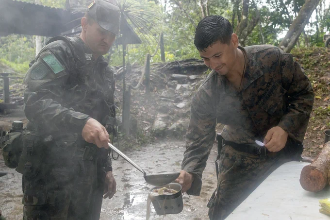 U.S. Marine Corps Sgt. Mark Rodriguez, right, a squad leader with Fox Company, 2nd Battalion, 25th Marine Regiment, 4th Marine Division, Marine Forces Reserve, is seen receiving "jungle soup" at the Jungle Amphibious Training School during Tradewinds 2023. The event took place at the Jungle Area Training Site in Guyana on July 23, 2023. Tradewinds, a U.S. Southern Command-sponsored exercise, aims to bolster partnerships and interoperability, advocate for human rights and enhance all participants' capacity to mitigate, plan for and react to crises and security threats. A native of South Hadley, Massachusetts, Rodriguez serves as a state trooper. He is a graduate of South Hadley High School. (U.S. Marine Corps photo by Cpl. Ryan Schmid)