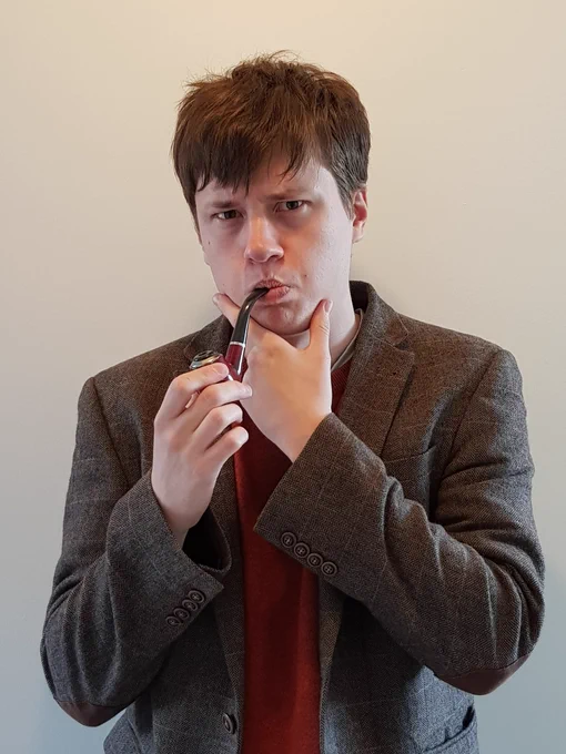 A young man wearing a tweed jacket pretending to smoke a pipe. He is apparently deep in thought.