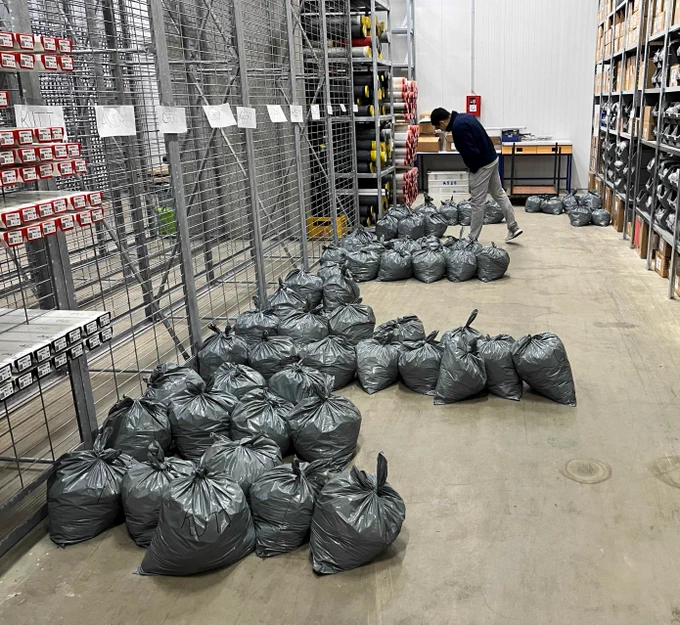 Trash bags filled with samples line the floor of the core repository. A scientist looks at a bag in the background.