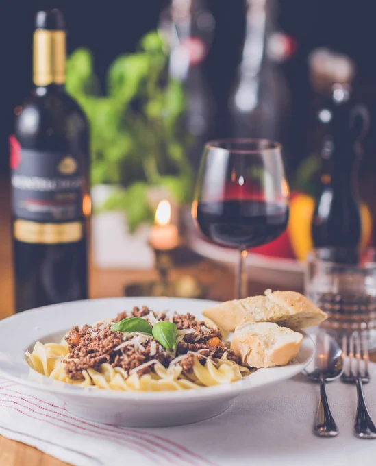 A bowl of pasta next to a glass of red wine.