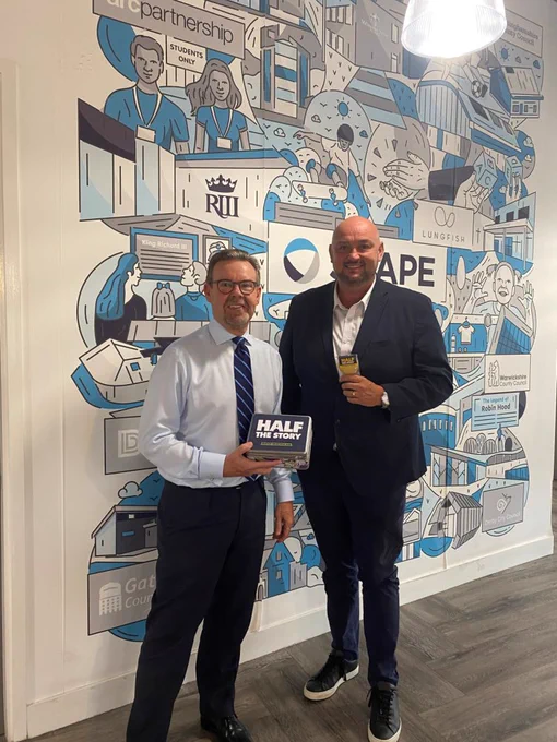 Mark Robinson and Andy Bacon from SCAPE, holding a plaque that says Half the Story and one of their biscuits.