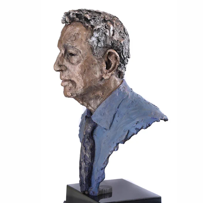 A bronze bust of Lord David Blunkett's head and shoulders. The bust depicts a man in his 70s with short hair. He wears a blue toned shirt with a black tie. 