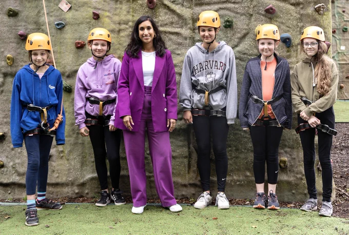 Minister Coutinho with children in front of a rock climbing wall.