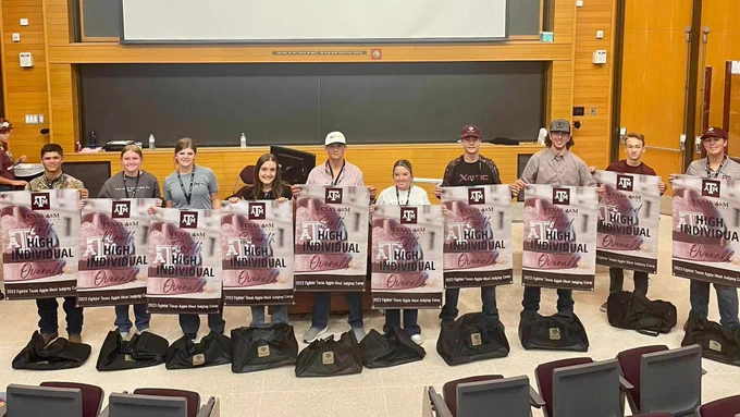 A group of students stand in a line holding award banners with camp bags on the ground.