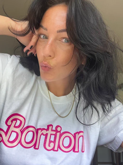 Liz wearing a white t shirt with pink Barbie style writing that says “Bortion”