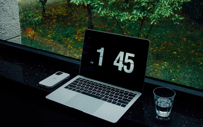 Ein Laptop und Handy liegen auf einer Fensterbank. Im Hintergrund sind Bäume und Wiesen.