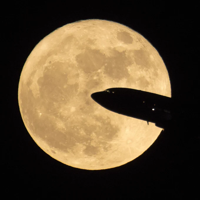 An aircraft taking off from Ronald Reagan National Airport is seen passing in front of the Moon as it rises, Sunday, Dec. 3, 2017 in Washington, DC. The nose of the airplane is silhouetted in front of a supermoon, glowing a pale gold color. The sky is black in the background. Credit: NASA/Bill Ingalls