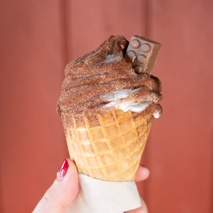 Soft serve ice cream sprinkled with chocolate and with a Lego brick shaped chocolate in the top, held in a hand with red painted nails, LEGOLAND Billund, Denmark