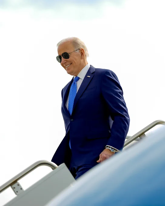 President Biden descending from the stairs of Air Force One, wearing sunglasses and a blue suit with a blue tie