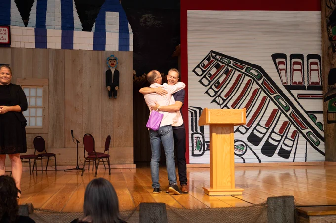 Two people congratulating each other on stage with a hug.