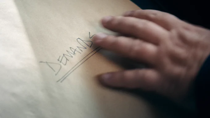 A hand hovers over a piece of paper with the word "Demands" written in all caps and underlined twice.