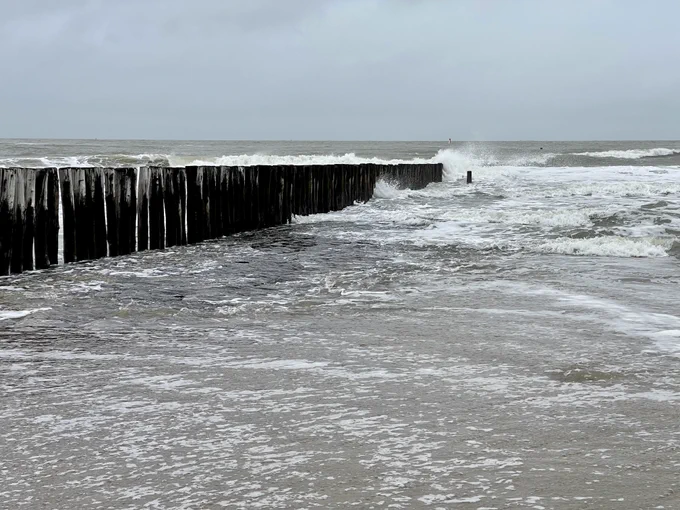 Foto van de zee met flinke golven tegen paaltjes.
