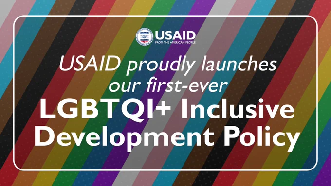 Pictogram with an inclusive pride flag background. Text reads: USAID Proudly Launches our First-Ever LGBTQI  Inclusive Development Policy