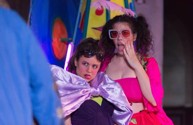 Two performers in bright costumes with shocked facial expressions