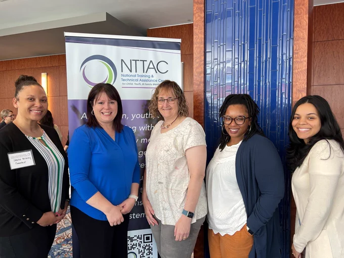 Five women pose in front of a NTTAC banner at the recent meeting for CONNECT grantees held in Baltimore, MD. Left to right is Jeana Bracey (CHDI), Bethany Zorba (DCF), Joy Kaufman (Yale, The Consultation Center), Taylor Ford (FAVOR), Marlene Gomez (CHDI).