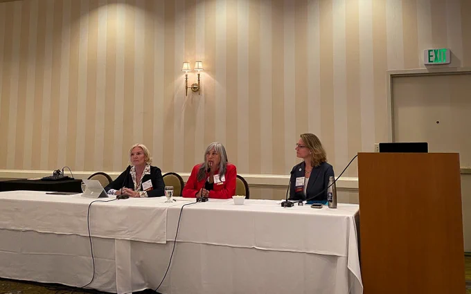 Three panelists sitting at a table with microphones indoors at the 2023 California Adaptation Forum.