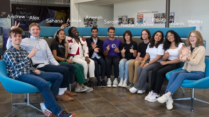 Group photo of Orbit Fab intern class of 2023 sitting in a half circle smiling, their names are labeled above and above and to the sides of the photo are their university insignia