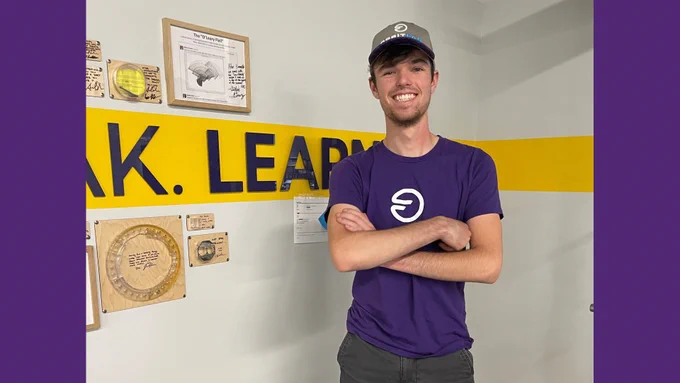 Image of Andrew Lana standing next to the wall of fail that says Build Break Learn Fly