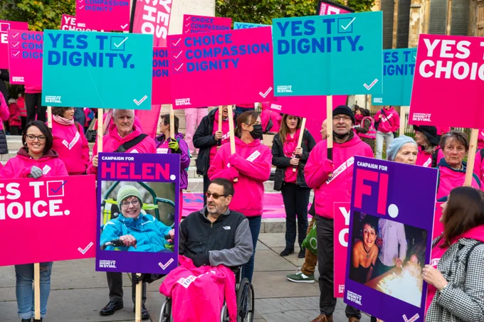 A group of people at a rally for assisted dying, holding placards with supportive messages