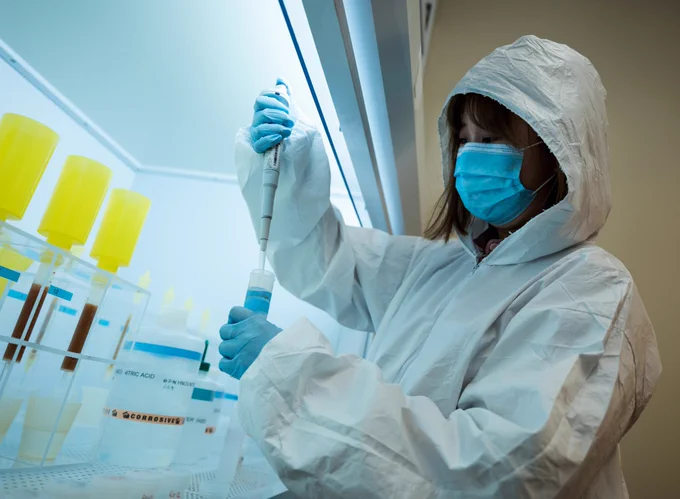 A researcher dressed in a full white protectant suit conducts an experiment. 