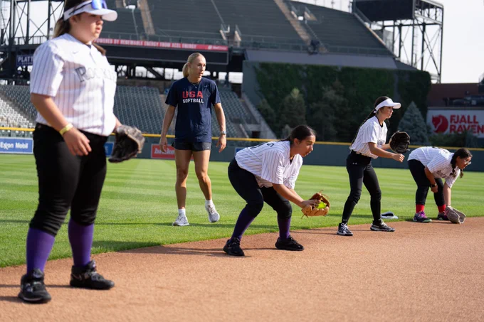 Skylar Wallace stands on the edge of the infield and provides instruction to four softball campers.