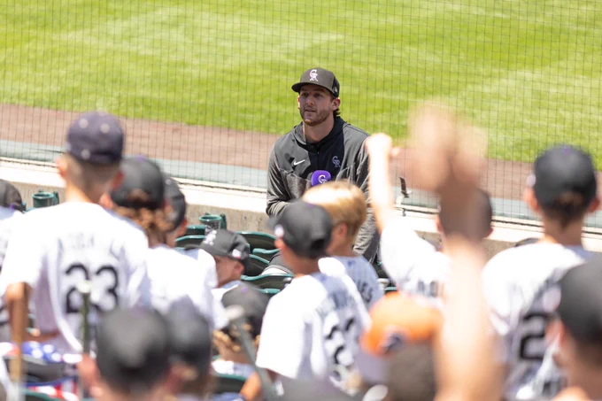 Ryan McMahon sits on the ledge with his back to the field and talks to a group of young campers.