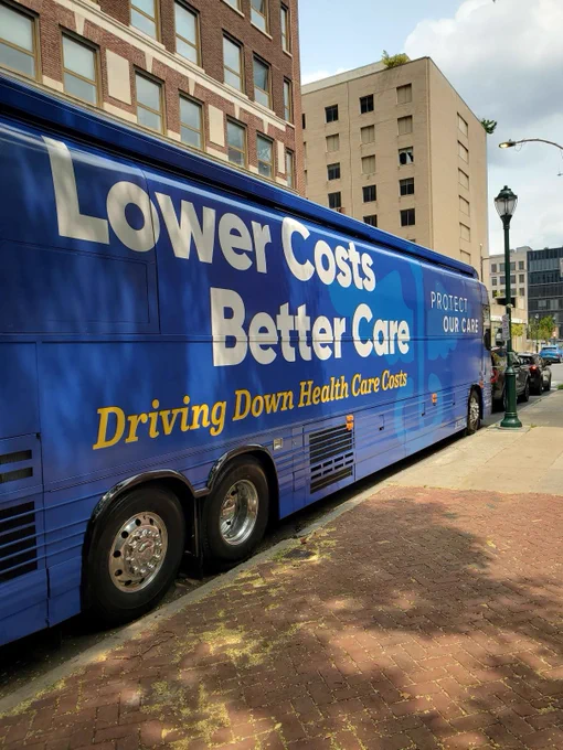 A blue bus has slogans on the side: Lower Costs. Better Care. Driving down health care costs. Protect our care.