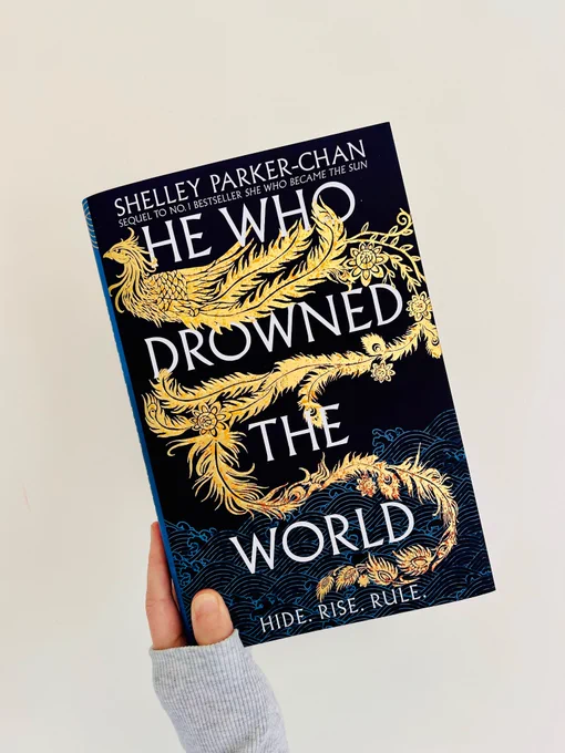 UK hardcover of He Who Drowned the World: a gold foil phoenix rising up from ominous dark blue waters rendered with a traditional Chinese wave pattern 