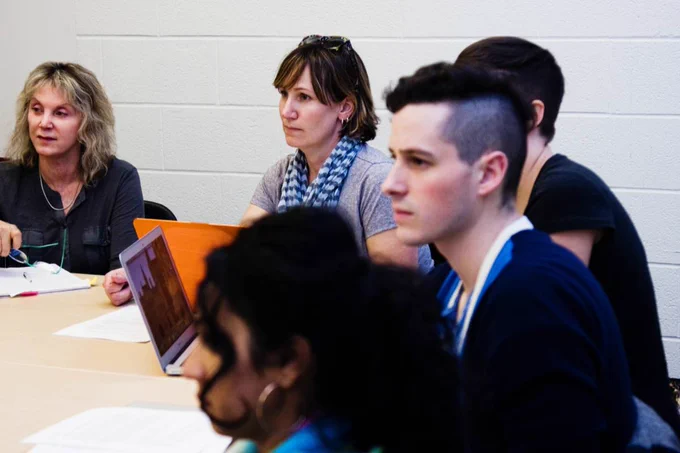 A group of people sitting at a table together, listening to a speaker.