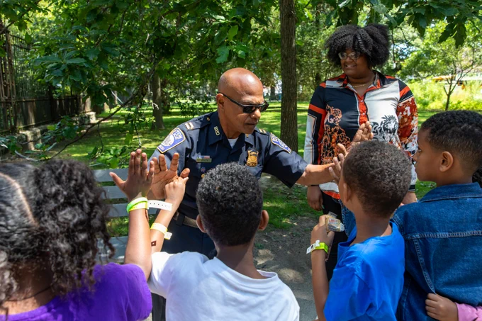 Local police officer surrounded by children and the Office of Neighborhood liaison Kiesha Santana.
